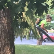 Female employee using a leaf blower to clear sidewalks in Greenfield