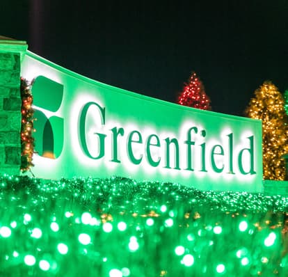 Greenfield Entrance sign illuminated with green holiday lights.