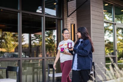 Two young women walking outside of Starbucks with their beverages, smiling at one another 