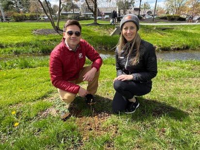 Man and Woman smiling in front of newly planted tree in Greenfield