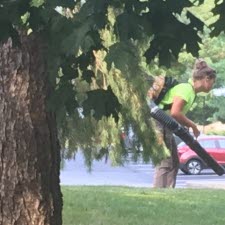 Female employee using a leaf blower to clear sidewalks in Greenfield